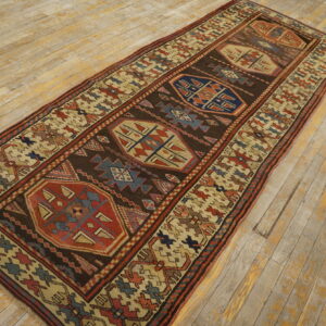Runner rug with dark brown field and geometric red, blue, and cream motifs on weathered wood floor.