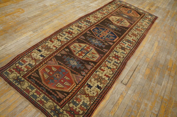 Runner rug with dark brown field and geometric red, blue, and cream motifs on weathered wood floor.