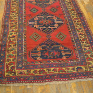 Red geometric rug with navy blue medallions and multi-colored borders lying on yellow wood planks.
