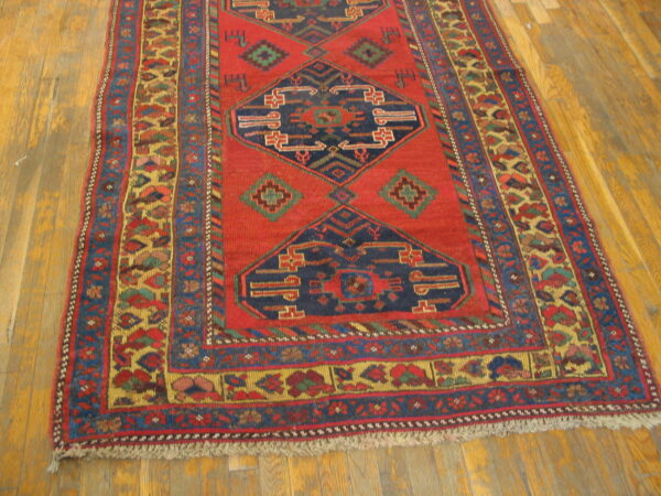 Red geometric rug with navy blue medallions and multi-colored borders lying on yellow wood planks.