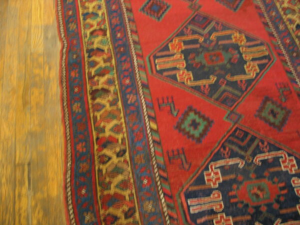 A red and navy geometric rug with detailed borders rests on golden-toned wood planks.