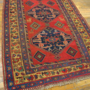 Red and blue geometric rug with medallions and colorful borders on light brown wood flooring.