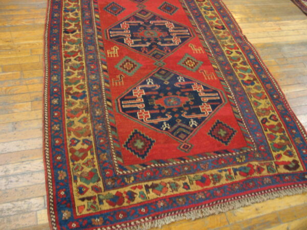 Red and blue geometric rug with medallions and colorful borders on light brown wood flooring.
