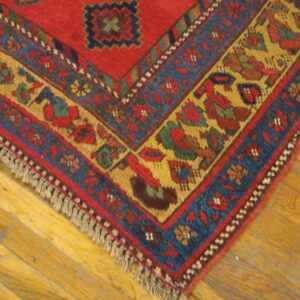 Close-up of a red, blue, and yellow patterned rug corner with fringe resting on hardwood planks.
