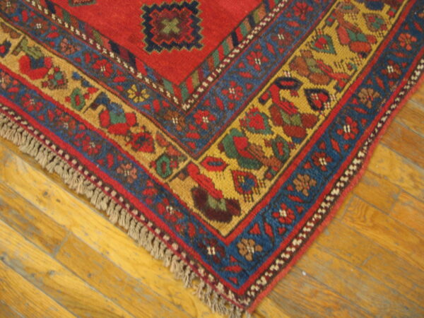 Close-up of a red, blue, and yellow patterned rug corner with fringe resting on hardwood planks.