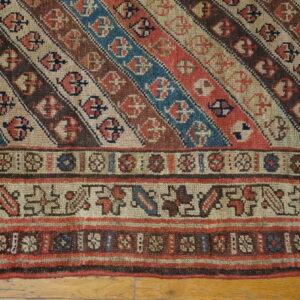 Diagonal striped rug in rust, blue, and brown with geometric borders rests on wood flooring.