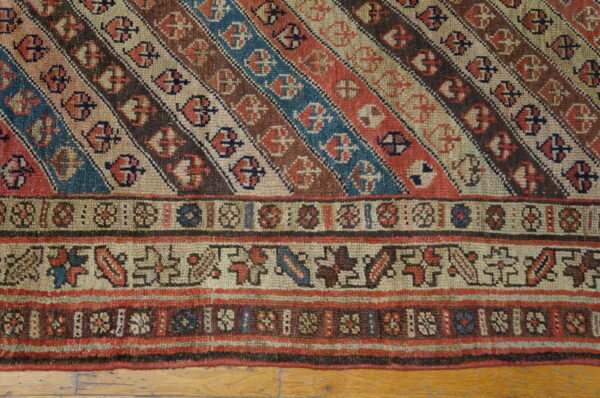 Diagonal striped rug in rust, blue, and brown with geometric borders rests on wood flooring.