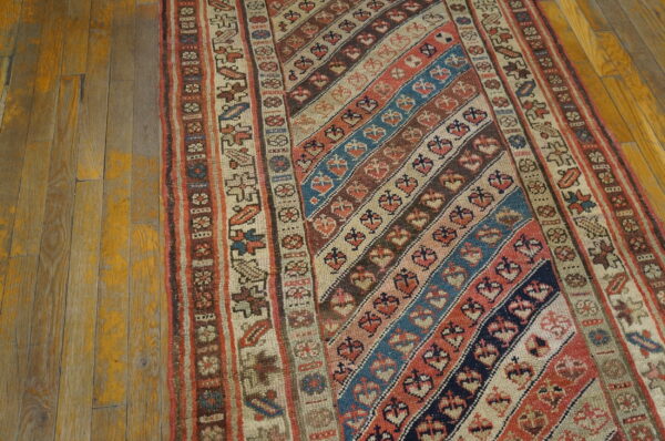 A low-pile runner rug with diagonal stripes of red, blue, and brown geometric patterns rests on worn wood.