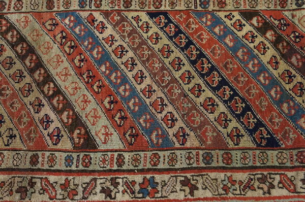 Diagonal stripes of terracotta, navy, and beige cover this rug section, framed by detailed geometric borders.