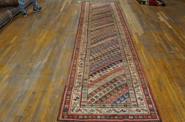 Low-pile runner rug with colorful diagonal stripes and a detailed border rests on a worn wood floor.