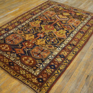 A geometric navy, orange, and gold patterned rug rests on light-colored, worn wood flooring.