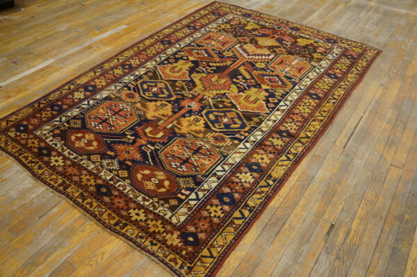 A geometric navy, orange, and gold patterned rug rests on light-colored, worn wood flooring.