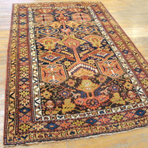 Detailed geometric rug in dark navy, orange, and olive green on a light wood plank floor.