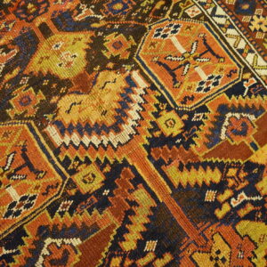 Geometric rug pattern featuring large orange and yellow medallions on a dark navy field, resting on wood floor.