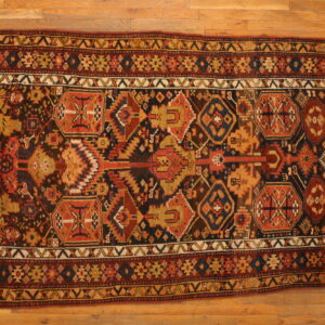 Geometric patterned rug in dark brown, red, gold, and blue rests on light natural hardwood flooring.