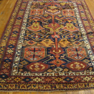 A complex geometric rug in navy blue, rust, and yellow covers light brown hardwood flooring.