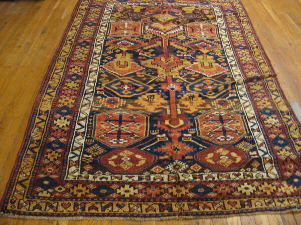 A complex geometric rug in navy blue, rust, and yellow covers light brown hardwood flooring.