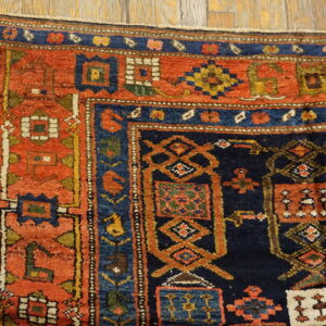 Rust and navy geometric tribal rug corner showing a thick pile texture on golden hardwood flooring.