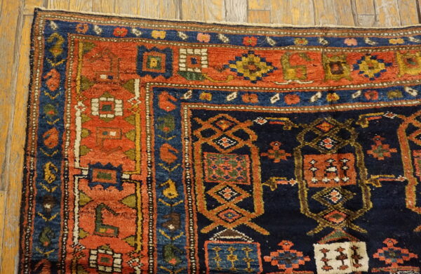Rust and navy geometric tribal rug corner showing a thick pile texture on golden hardwood flooring.