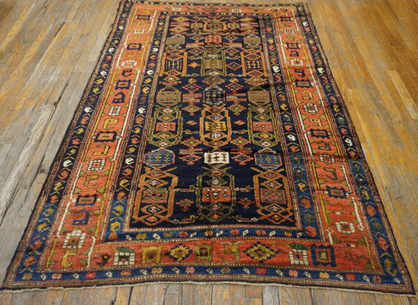 Low-pile tribal rug featuring bold navy, orange, and yellow geometric designs resting on rustic wood plank flooring.