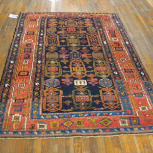 Traditional geometric rug with a navy center and wide coral border lies on light brown wood flooring.