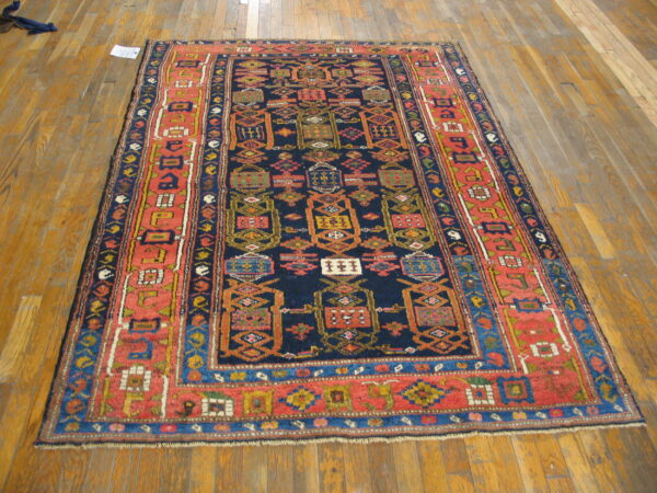 Traditional geometric rug with a navy center and wide coral border lies on light brown wood flooring.