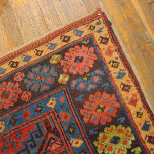 High-pile rug corner featuring red, blue, and tan floral geometric patterns rests on wood planks.