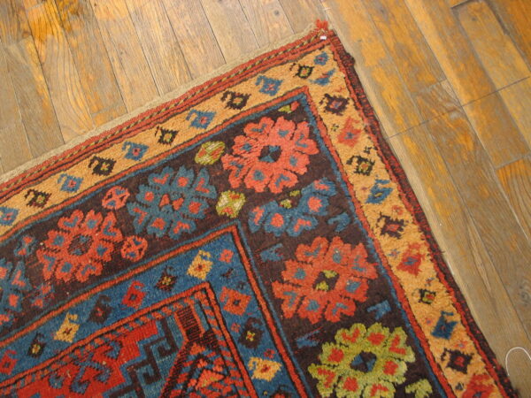 High-pile rug corner featuring red, blue, and tan floral geometric patterns rests on wood planks.