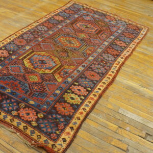 Runner rug with intricate red, blue, and brown traditional geometric designs lies on worn yellow plank flooring.