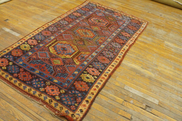 Runner rug with intricate red, blue, and brown traditional geometric designs lies on worn yellow plank flooring.