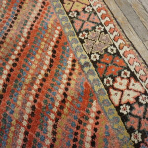 Red and multicolored rug with a geometric dotted field and complex patterned borders on gray wood floors.