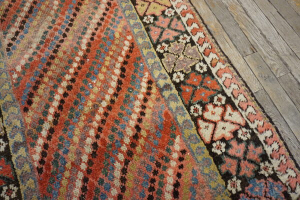 Red and multicolored rug with a geometric dotted field and complex patterned borders on gray wood floors.