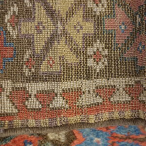 Geometric, low-pile rug in brown, gold, and white layered above a higher-pile rug with blue and red patterns.