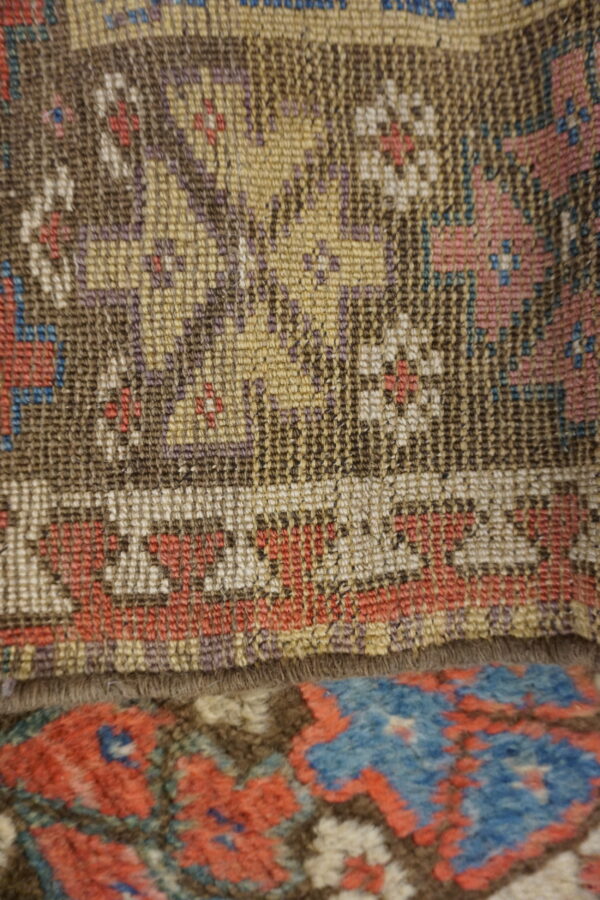 Geometric, low-pile rug in brown, gold, and white layered above a higher-pile rug with blue and red patterns.