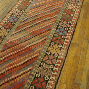 Distressed colorful runner rug featuring geometric and diagonal dot patterns displayed on worn wooden floors.