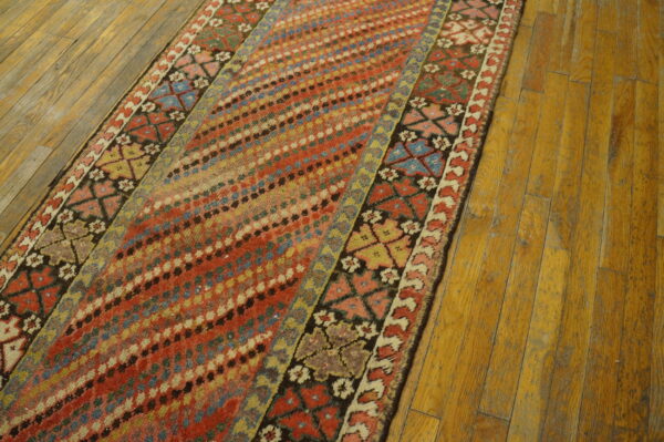 Distressed colorful runner rug featuring geometric and diagonal dot patterns displayed on worn wooden floors.