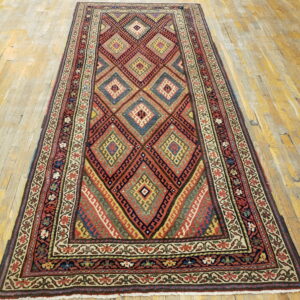 A runner rug with red, blue, and gold geometric patterns is placed on light, worn hardwood flooring.