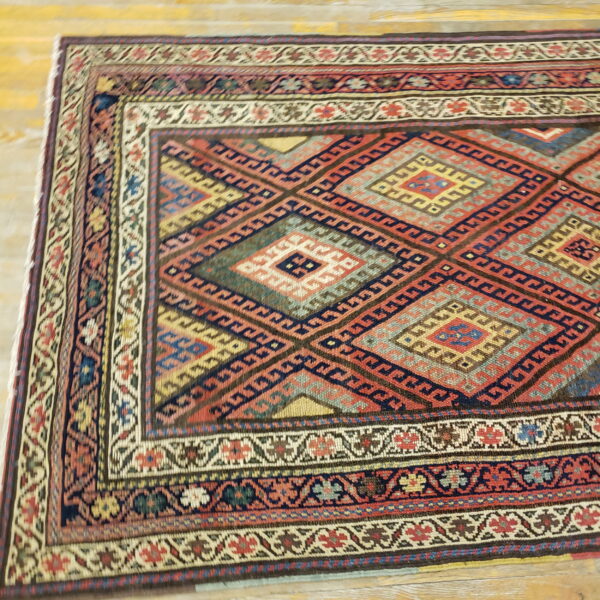 Detailed geometric rug in red, navy, green, and gold colors rests on light wood planks.