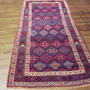Red and blue geometric runner rug with complex borders laid over light wood planks.