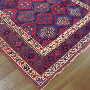 Red and navy geometric rug featuring medallion patterns and tan borders lies on light wood plank flooring.