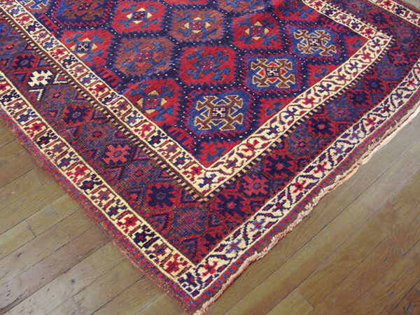 Red and navy geometric rug featuring medallion patterns and tan borders lies on light wood plank flooring.
