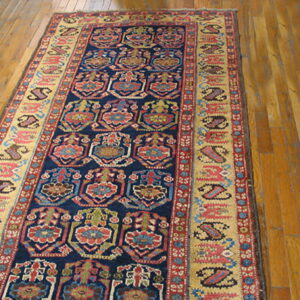 Geometric runner rug with a navy field and gold border, featuring repeating multi-colored motifs on wood plank flooring.