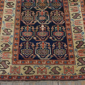 Navy and red geometric runner rug with a tan border and stylized paisley shapes on rustic wood floorboards.