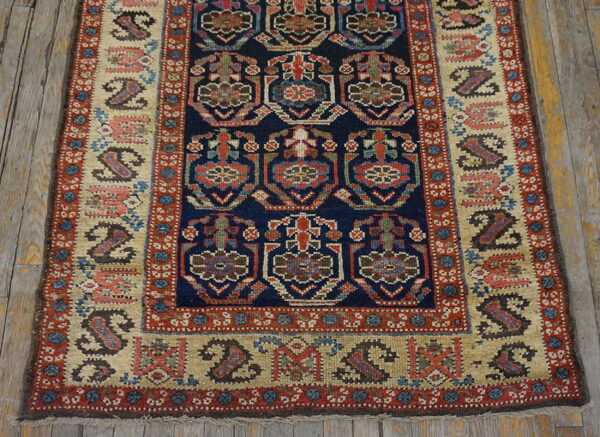Navy and red geometric runner rug with a tan border and stylized paisley shapes on rustic wood floorboards.