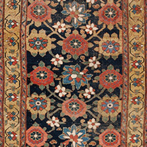 Low-pile runner rug featuring red and blue florals on a dark blue background covers old wood floors.