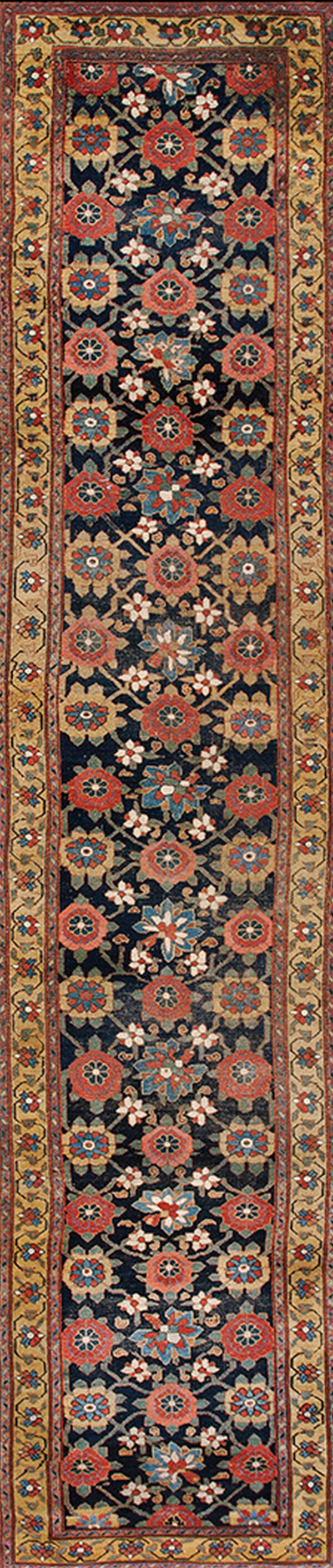 Low-pile runner rug featuring red and blue florals on a dark blue background covers old wood floors.