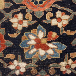 Navy blue rug detail with dense floral patterns in terracotta, cream, light blue, and sage green.