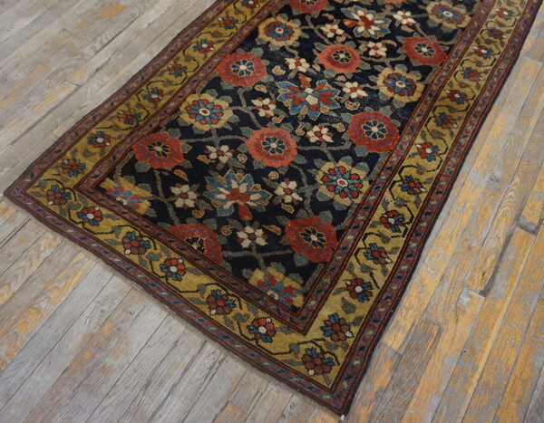 A navy rug with dense red, blue, and gold floral patterns lies diagonally on distressed wooden planks.