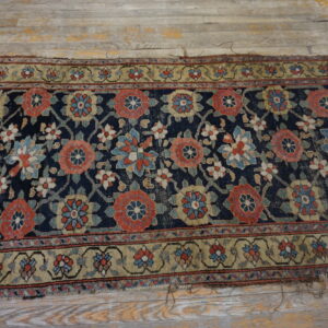 A distressed floral runner rug with a navy field and tan border rests on worn gray wood flooring.