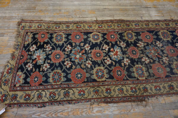 A distressed floral runner rug with a navy field and tan border rests on worn gray wood flooring.